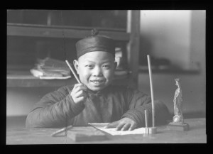 Smiling_boy_seating_at_a_table_writing,_China,_ca._1918-1938_(MFB-LS0248A)
